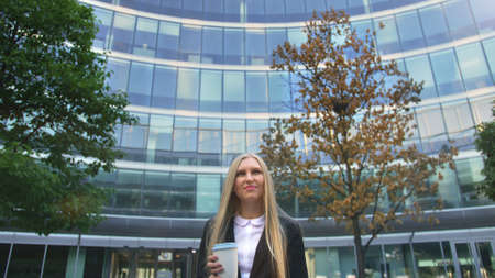 From below of serious blond executive woman in suit having coffee in paper cup looking away on street.の写真素材