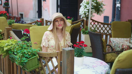 Smiling woman in outside restaurant. Cheerful young woman sitting at table in outside restaurant on cozy street.の写真素材