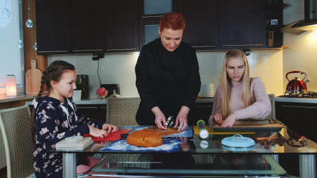Women baking gingerbread cookies in the kitchen at home. Young girl helping them and observing the...