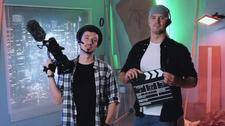 Camera man and producer assistant smiling to the camera and showing their equipment: movie camera and movie clapper board.の写真素材
