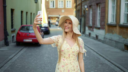 Woman taking selfie on street. Cheerful young woman walking on old European town street and taking selfie with smartphone.の写真素材