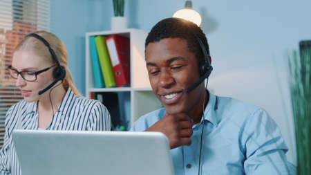 Close-up of friendly african man working in call center. He answering international call in a...