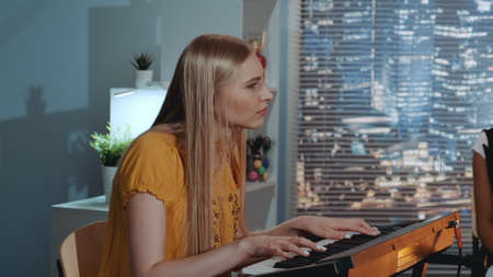 Vocalist blonde singing a song and playing the keyboard during rehearsal of her band in home recording studio. There are skyscrapers in the background.の写真素材