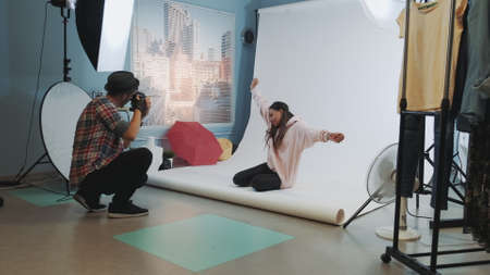 Backstage of the photo shoot: black model sitting on the floor and posing for a photographer. There is a modern equipment around in studio photo shoot.の写真素材