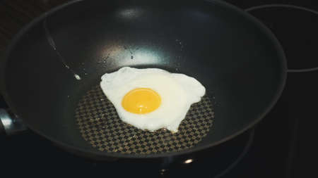 Close-up of cooking egg on a frying pan to breakfast dish in kitchenの写真素材