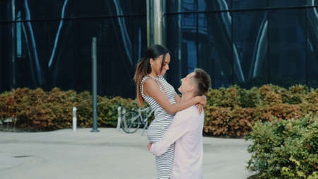 Multiracial family concept: husband spinning around his wife while walking down the street near big office centre one summer dayの写真素材