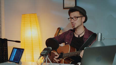 Cheerful young musician playing the guitar and singing into microphone in home studio. Musical instruments and hobby concept.の写真素材