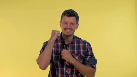 Excited young man yelling and raising fists in cheer on yellow background. He supporting and encouraging somebody.の写真素材