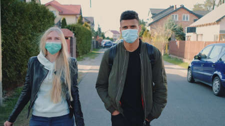 Multiethnic man and woman in medical masks walking down the street in housing estate. They spending their free time together.の写真素材