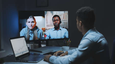 Mixed-race colleagues working home on quarantine by making common video call on a big monitor. They working late at night.の写真素材