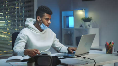 Multiracial man on quarantine working home late at night. He drinking coffee and working on computer.の写真素材