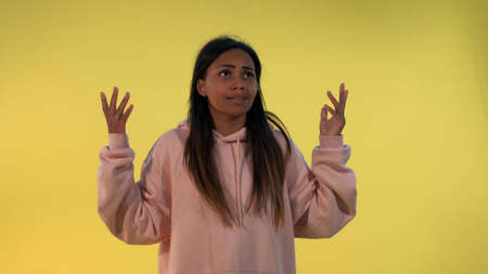 Upset african woman spreading hands to the sides and shooting herself in the head with finger gun gesture. There is a yellow background.の写真素材
