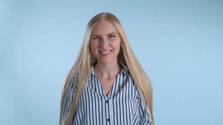 Attractive young lady biting her lip and smiling. Blue background.の写真素材