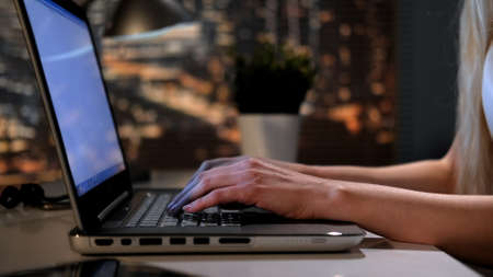 Close-up of womans hands writing something on laptop in office in the eveningの写真素材