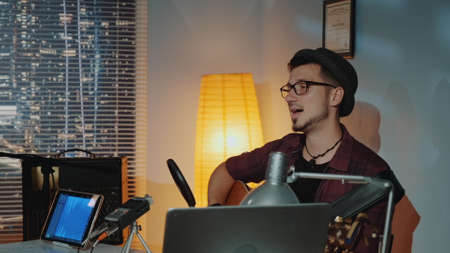Home recording studio: young musician in hat singing and playing guitar. In front - music recording equipment.の写真素材