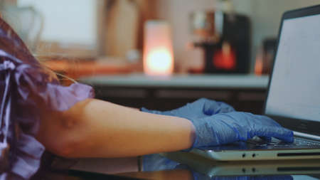 Close-up shot of womans hands in medical gloves typing on keyboard. In the background warm lights.の写真素材