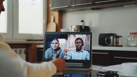 Close-up shot of Multiracial colleagues working home on quarantine by making common video call by computer. Black man sitting in the kitchen and writing.の写真素材
