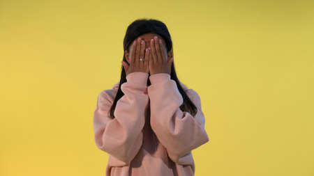 Attractive black woman covering her face with hands, then opening it and smiling. Yellow background.の写真素材