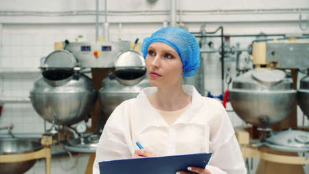 Controller checking confection factory. Young female in uniform making notes in folder while inspecting laboratory in confection factory. Candy factory.の写真素材