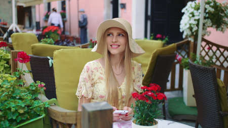 Smiling woman in outside restaurant. Cheerful young woman sitting at table in outside restaurant on cozy street.の写真素材