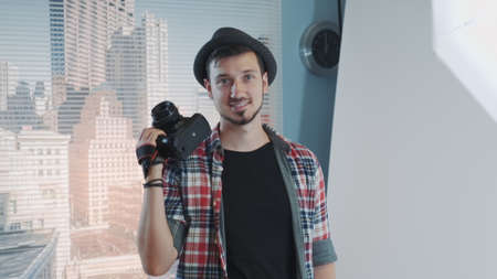 Portrait of young professional photographer in casual clothes with his camera smiling and posing. There are skyscrapers in the background.の写真素材