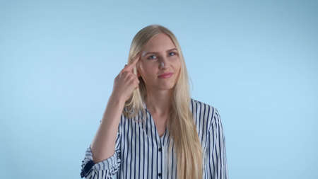 Attractive woman twisting her index finger at temple on blue background. She looking at camera with disagreement.の写真素材