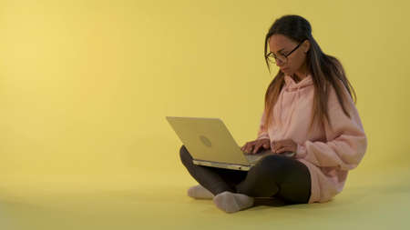 Smart african girl working on the computer on yellow background. She sitting on the floor.の写真素材