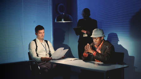 Police detective questioning suspect black man in interrogation room. Female assistant making notes of the interrogation.の写真素材