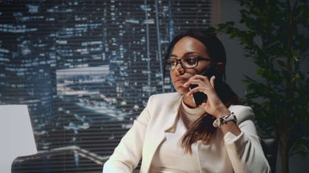 Close up of multiracial business lady speaking by smartphone with a client at her office. She is in black eyeglasses.の写真素材