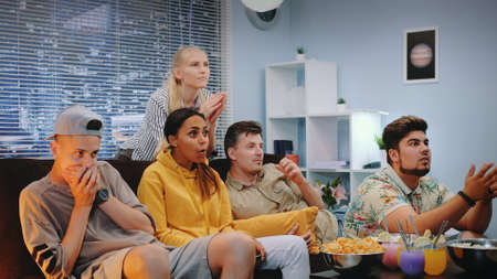 Best friends watching TV and celebrating success for their favourite team. They are extremely happy for the winner, screaming, jumping and raising clenched fists.の写真素材