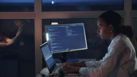 Side view of african american female engineer working on computer in electronics laboratory. Doing Development of Software and Hardware. She wearing a lab coatの写真素材