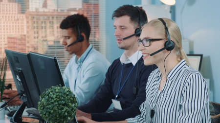 Medium shot of female customer service working in busy call center by talking to the international client. Her mixed-race team also taking calls.の写真素材