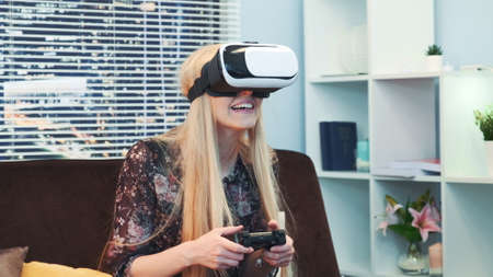 Joyful woman playing a game with joystick in virtual reality goggles on Christmas. There are skyscrapers in the background. Future technology concept.の写真素材