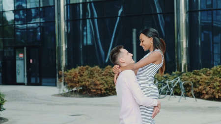 Happy boyfriend holding his black girlfriend in his hands and spinning around outdoors. An office building is in the background.の写真素材