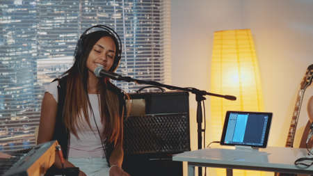 Attractive mixed-race girl emotionally singing into microphone in home studio with musical equipment in the background. Evening rehearsal.の写真素材