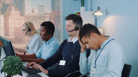Multiracial call center agent feeling exhausted and broken-down after telephone call with the client. He working with mixed-race team in modern office.の写真素材