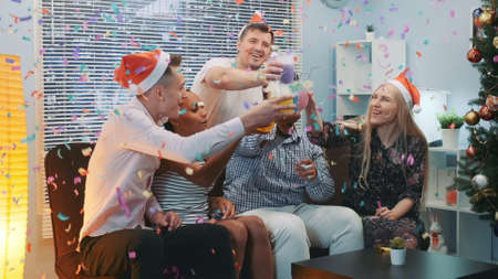 Close up of cheerful company celebrating Christmas in confetti blowing while making cheers and blowing party whistles at home.の写真素材