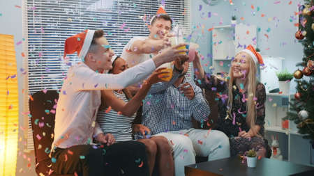 Close up of cheerful company celebrating Christmas in confetti blowing while making cheers and blowing party whistles at home.の写真素材