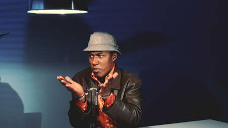 Young black man in handcuffs refusing accusation in his address during police interview in interrogation room.の写真素材