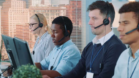 African customer service representative working on multiracial team of modern call center. Teamwork activity desk in busy office.の写真素材