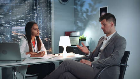 Psychologist therapy session: businessman sharing his problems with specialist in psychological health in modern comfortable office in the eveningの写真素材