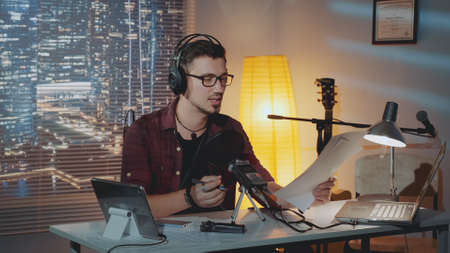 Home recording studio: the speaker in headphone reads the story into the microphone. There is a computer and other recording equipment on the table.の写真素材