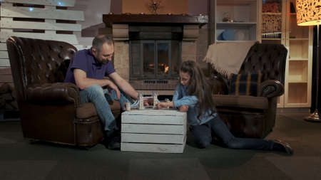 Small daughter and father playing together in a big comfortable living room near the fireplace in the evening. They have fun.の写真素材