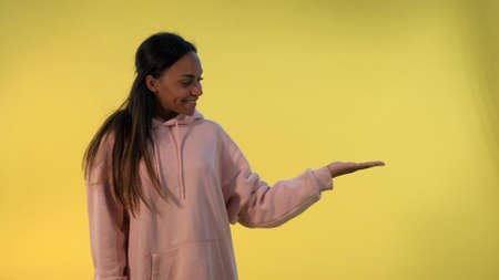 Beautiful african woman presenting something on empty hand with yellow background. She looking on copy space for product.の写真素材