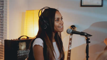 Close-up of beautiful smiling girl in headphone singing her favourite song on the rehearsal in home studio in the evening.の写真素材