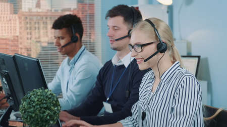 Medium shot of female customer service working in busy call center by talking to the international client. Her mixed-race team also taking calls.の写真素材