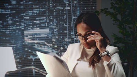 African american business woman in eyeglasses reading document at the office. There are skyscrapers in the background.の写真素材