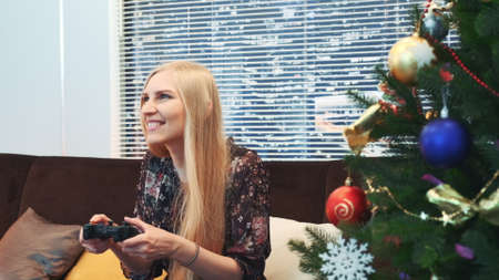 Close up of excited woman loses game on joystick near the Christmas tree. There are skyscrapers in the background.の写真素材