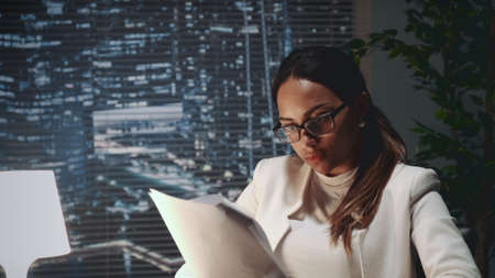 African american business woman in eyeglasses reading document at the office. There are skyscrapers in the background.の写真素材