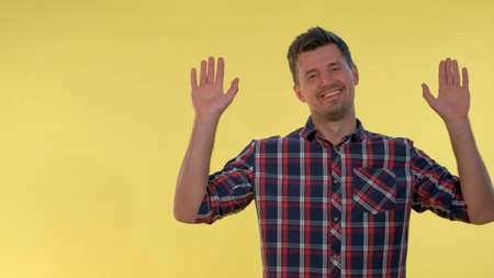 Happy young man covering his face with hands, then opening it and smiling. There is yellow background.の写真素材
